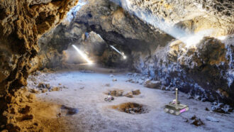 An illustration of a rover exploring a lava tube with light streaming through the top