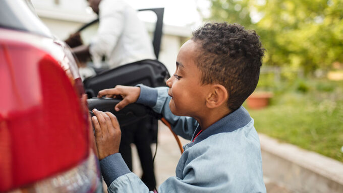 a photo of a Black boy plugging a red EV at a charging station