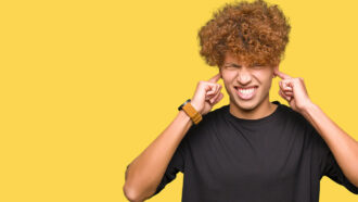 a young man with an afro plugs his ears and grimaces