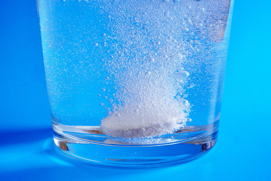 a photo of an Alka-Seltzer tablet starting to fix at the bottom of a clear glass full of water