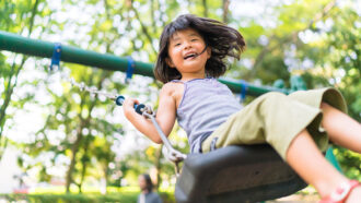 A Girl looks happy swinging on a swingset surrounded by trees