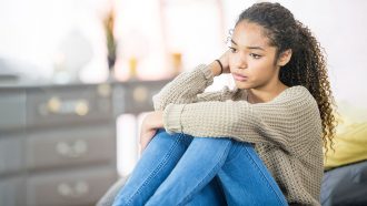 a photo of a curly-haired girl resting her arms on her knees and looking sad