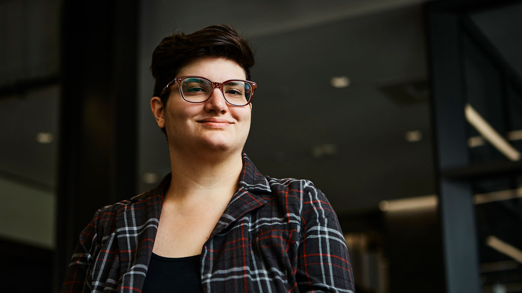 Astrophysicist Mallory Molina is wearing a red plaid shirt. They have short black hair and are wearing glasses with red frames.