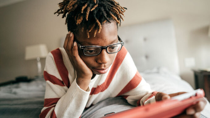 teen reading on a tablet lying in bed