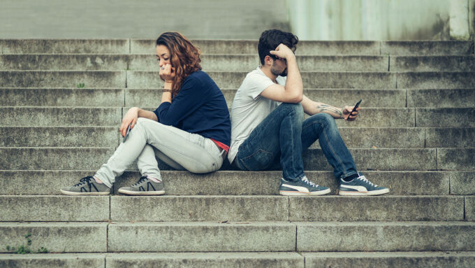 a young woman and a young man sitting on stairs back to back and looking upset